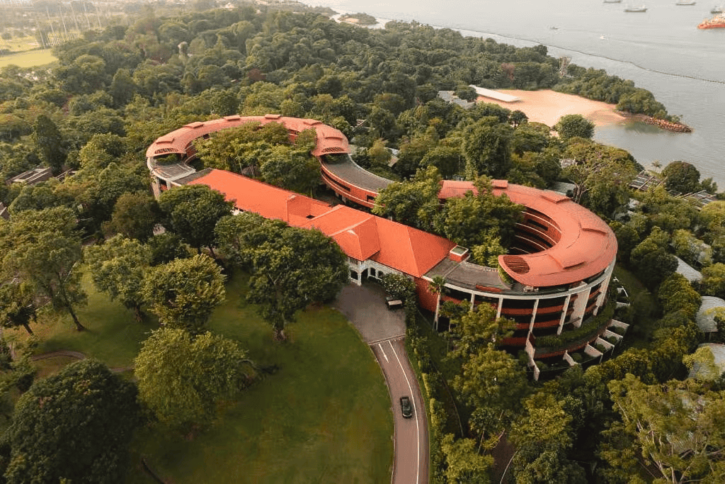 Aerial view of Capella Singapore on Sentosa Island, featuring distinctive curved architecture, terracotta rooftops and lush tropical greenery.