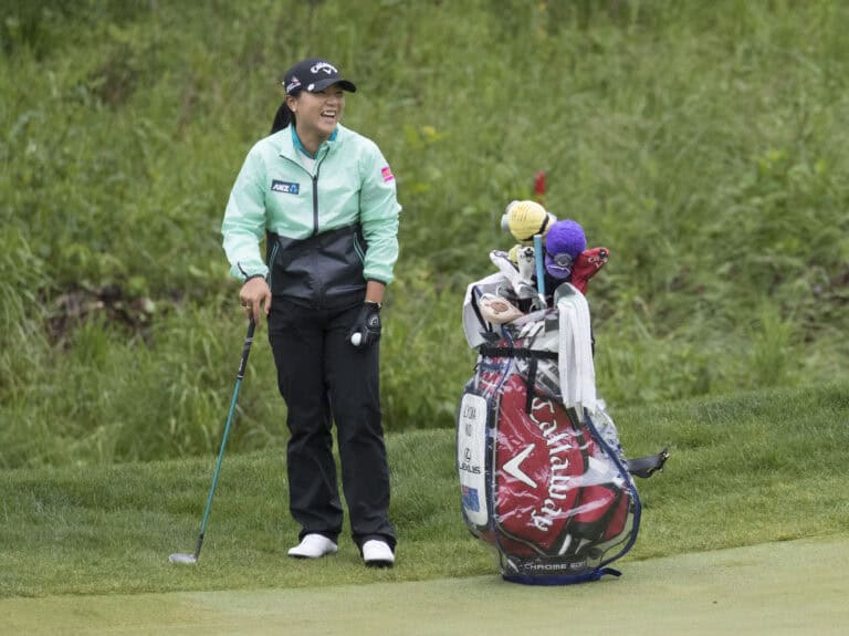 Lydia Ko smiling beside her golf bag at the LPGA Kingsmill in 2016, wearing a mint-green jacket and black cap.