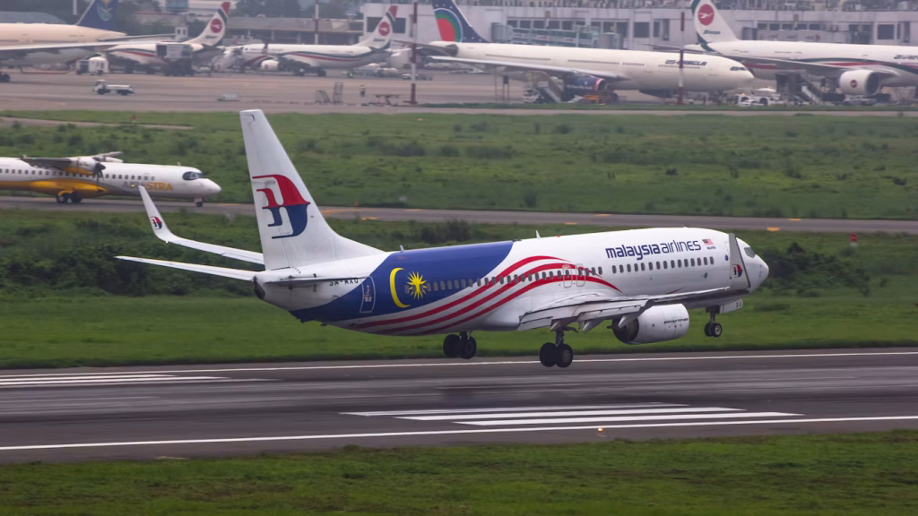 Malaysia Airlines aircraft landing on a runway with other passenger planes in the background.