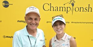 Mark Siegel and Lydia Ko holding Asian GOLF & More magazine in front of a yellow Maybank Championship backdrop.