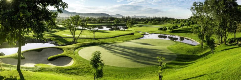 Panoramic view of Black Mountain Golf Club in Hua Hin, Thailand, featuring a lush putting green, sand bunkers, water hazards and mountain scenery.