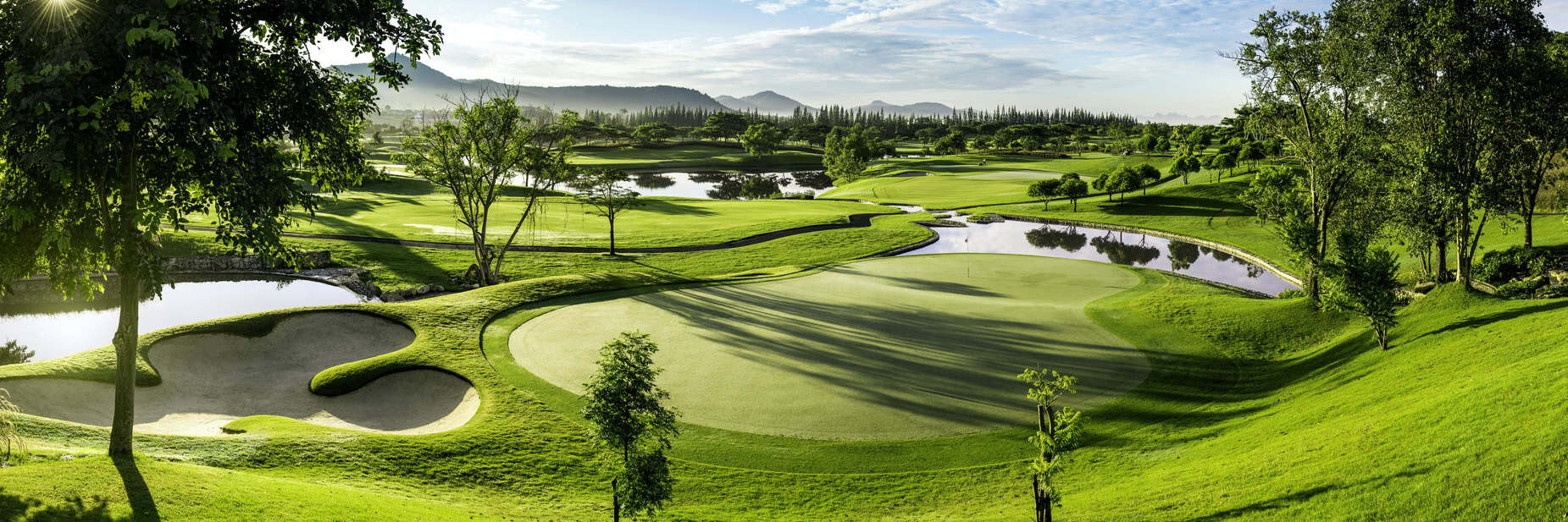 Panoramic view of Black Mountain Golf Club in Hua Hin, Thailand, featuring a lush putting green, sand bunkers, water hazards and mountain scenery.
