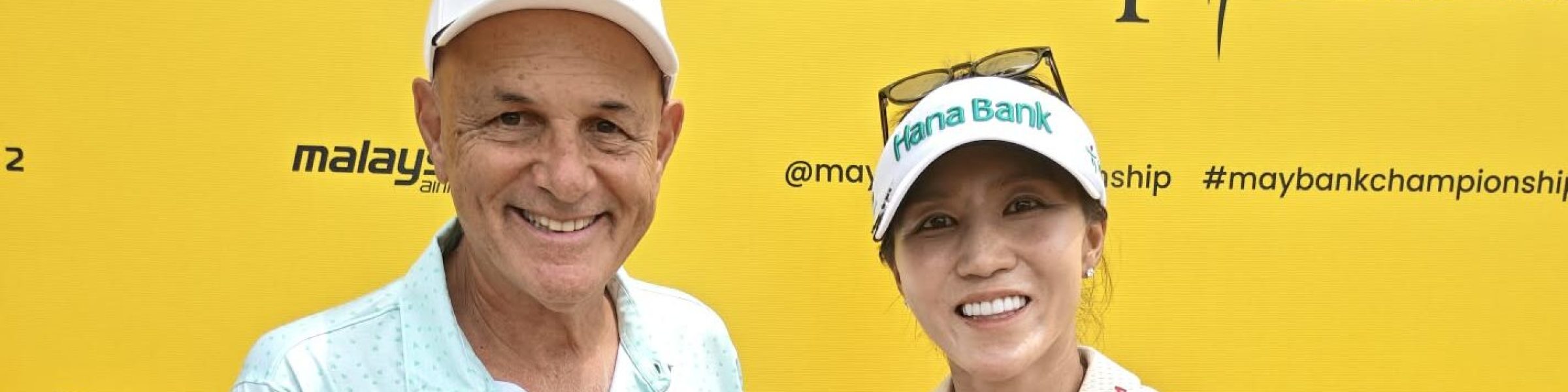 Mark Siegel and Lydia Ko holding Asian GOLF & More magazine in front of a yellow Maybank Championship backdrop.