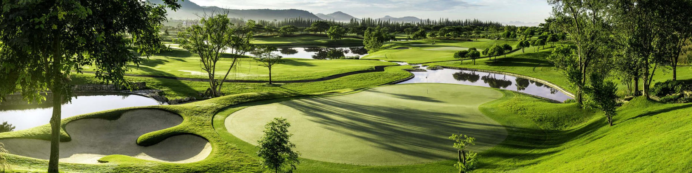 Panoramic view of Black Mountain Golf Club in Hua Hin, Thailand, featuring a lush putting green, sand bunkers, water hazards and mountain scenery.